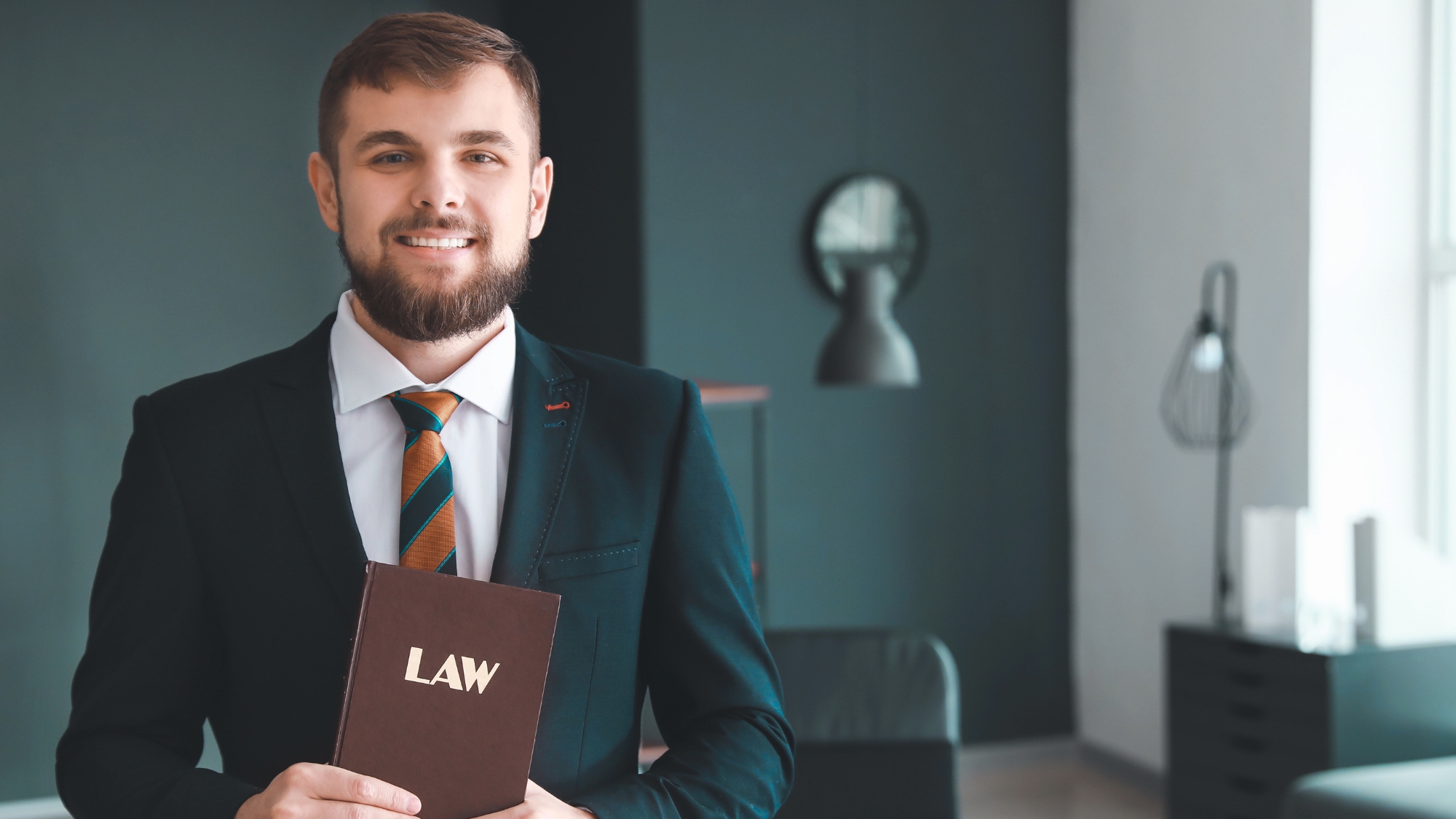 ung advokat med engelsk lovbok ser mot kamera. Bakgrunn kontor.