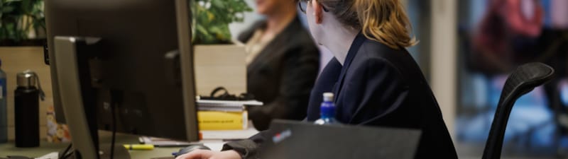 Bilde av to ansatte som jobber med datamaskinen sin og ser vekk fra kameraet